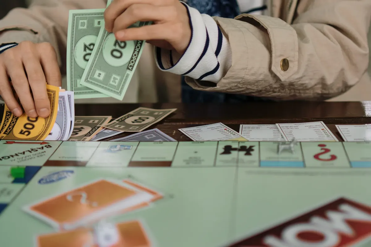 ボードゲームのセッション中に手でモノポリーのお金数える様子、楽しさと戦略を強調しています。