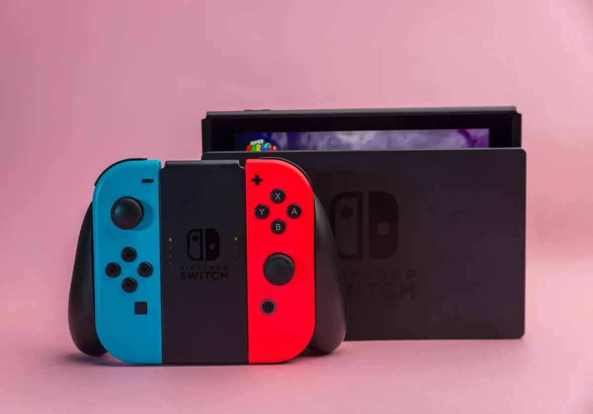 Close-up of Nintendo Switch console with red and blue Joy-Con controllers on pink background.