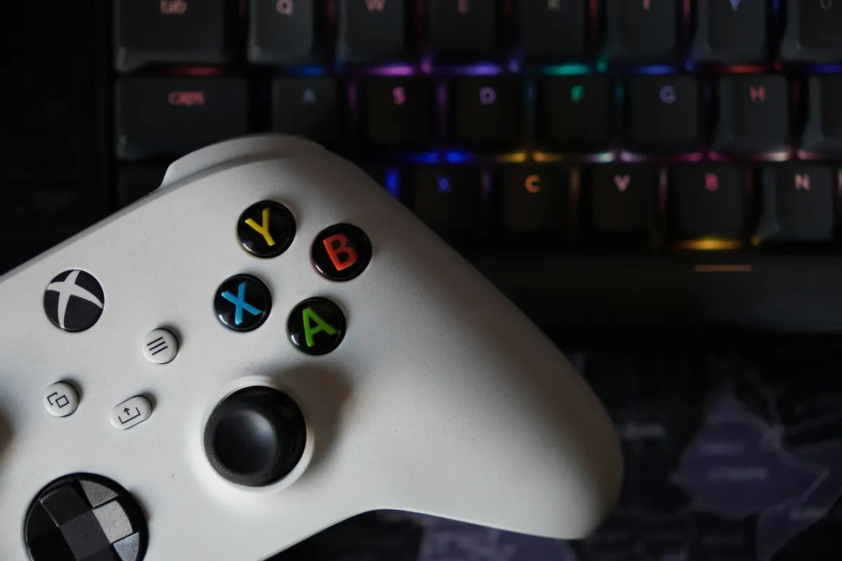 Game controller beside illuminated RGB keyboard, highlighting technology and gaming equipment.